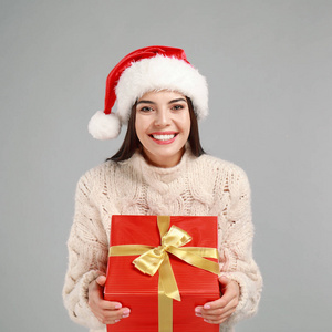 快乐的年轻女子戴着圣诞帽，灰色背景上有圣诞礼物
