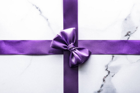 Purple silk ribbon and bow on luxury marble background, holiday 