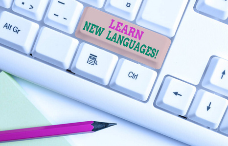 显示学习新语言的文字标志。概念照片开发能力，在外国语言白色电脑键盘上与空白笔记纸白色背景键复制空间。