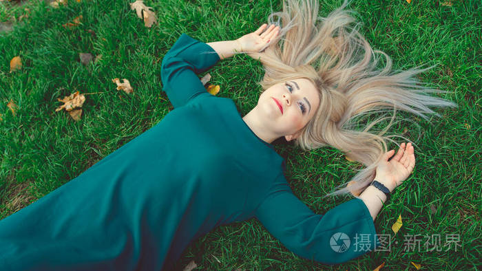 一幅美丽女孩的画像躺在草地上一个迷人的女人躺在长着黄叶的绿草上