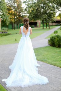 高加索新娘站在花园里穿着白色长裙的后视图。