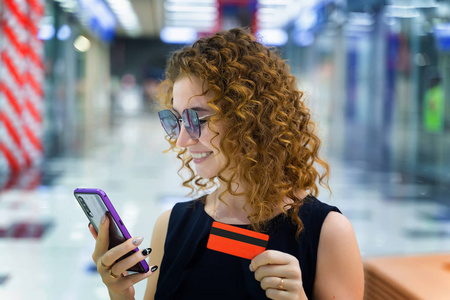 Beautiful sexy girl in the mall holds a credit card and a phone 