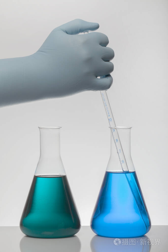 一只手拿着实验室手套的手混合着化学物质.实验室瓶子里的液体.