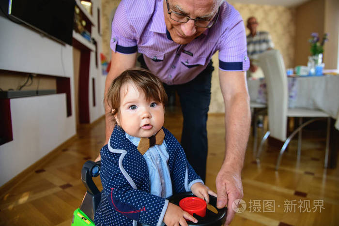 爷爷在玩具车里给孙子滚来滚去。祖父和孙子的重新定向。周末快乐概念。快乐的爷爷和孙子在家散步。