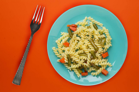 盘子里的意大利面和钛色背景的蔬菜。橙色背景的地中海食物。健康食品