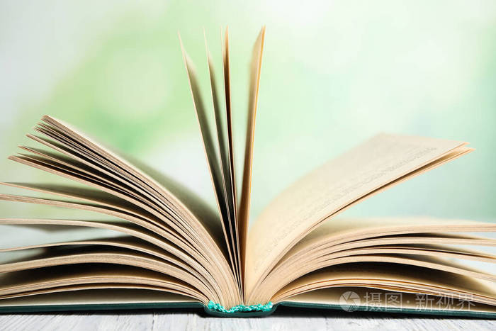 在模糊的绿色背景下白色木桌上打开一本书特写