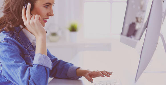 快乐迷人的年轻女子坐在办公室里用耳机用笔记本电脑工作