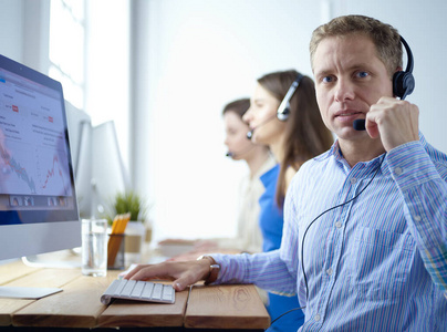 年轻的呼叫中心接线员戴着耳机和同事在办公室后台工作