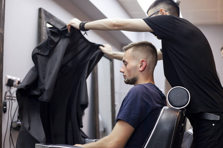 哈萨克年轻的理发师在理发店工作，小伙子坐在理发店剪短发