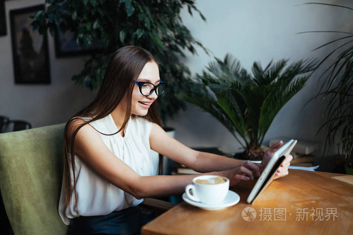 一个戴着眼镜的学生看着咖啡桌旁的平板电脑，他的脸被一个找到解决办法的人的微笑所照亮