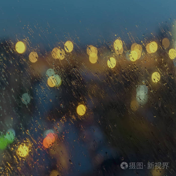 抽象模糊的城市夜光背景下的雨。雨点打湿了窗户，街上乱七八糟。天气季节现代城市的概念