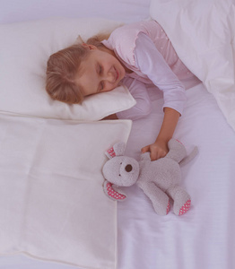 小女孩和玩具泰迪熊睡在床上。