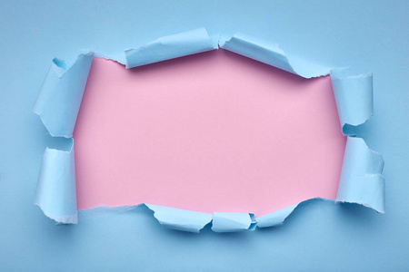 蓝纸上的洞。撕裂。粉红色背景。抽象背景。