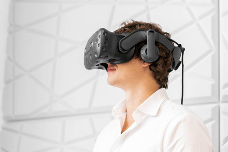 年轻兴奋的男子戴着虚拟现实护目镜在现代明亮的合作办公室。虚拟现实体验。