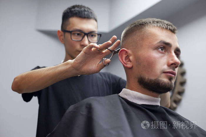 小伙子在理发店理发年轻的哈萨克理发师用剪刀和梳子手工理发师傅在