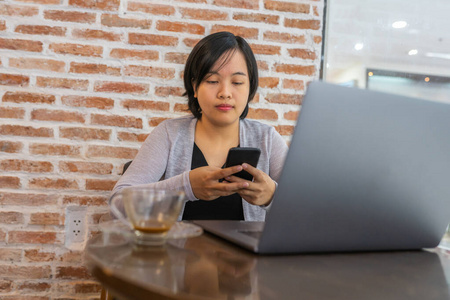 年轻的短发女人在咖啡店用手机和笔记本电脑