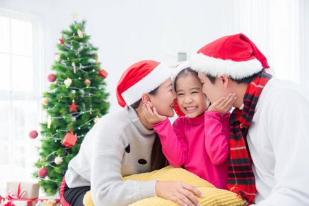 Little asian girl smiling while her parents kissing her in room 