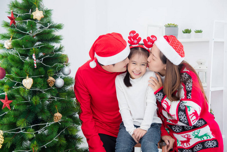 Little asian girl smiling while her parents kissing her in room 