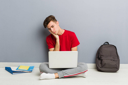一个年轻的学生拿着笔记本电脑坐在家里的地板上