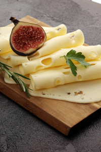 用欧芹放在木制托盘上的奶酪片。高达奶酪