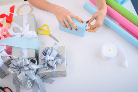 女人用新年礼物包装盒子。女性手特写。为圣诞节准备一个惊喜。包装纸和丝带。