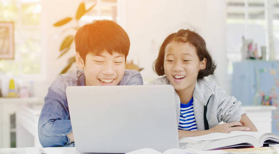 Young asian boy and girl playing with laptop computer at home. 