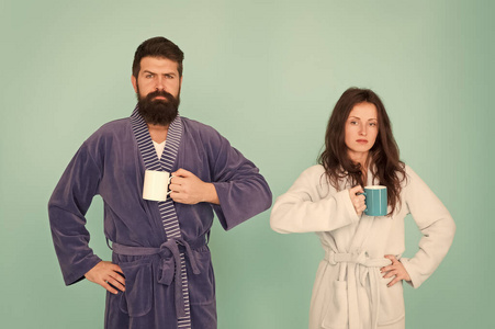 每天早晨从咖啡开始。一对夫妇穿着浴袍拿着杯子。早餐概念。留胡子的男人和昏昏欲睡的女人喜欢喝早茶或咖啡。穿着浴衣的家伙端着茶咖啡。