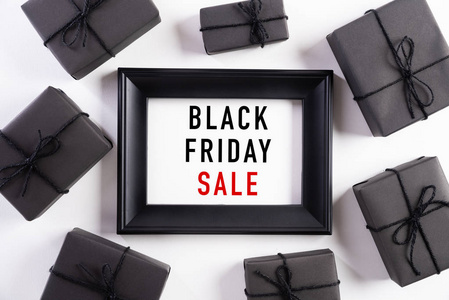 黑色星期五销售文本在白色相框上的俯视图，黑色礼品盒和白色背景上的圣诞球和浆果。购物理念和黑色星期五的构成。