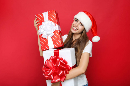 Beautiful woman wearing santa hat and holding gift boxes on red 