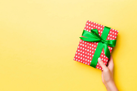 Woman arms holding gift box with colored ribbon on yellow table 