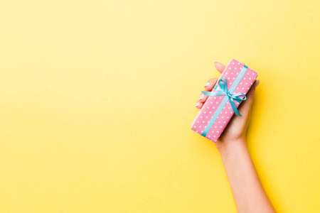 Woman arms holding gift box with colored ribbon on yellow table 