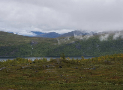 Kungsleden的Lapland nature徒步旅行小径，有绿色的山脉Teusajaure湖岩石巨石秋天的彩色灌木丛