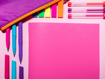 在粉红色的桌子上有一本粉红色的笔记本，彩色钢笔和一把双桅帆船