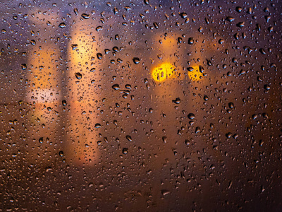 夜幕中城市的灯光在雨中的玻璃后面布满了水滴。抽象模糊的背景。