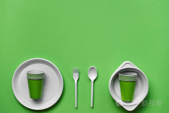 彩色塑料一次性餐具，绿色背景，带复印空间。野餐用具的概念。俯视图。选择性聚焦。特写。