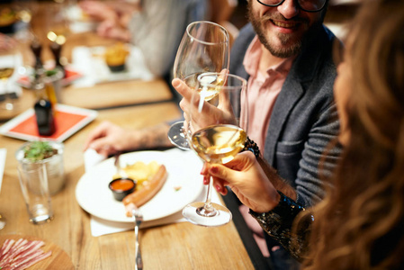 可爱的白人夫妇坐在餐厅里喝酒欢呼的剪贴照片。背景是他们的朋友。