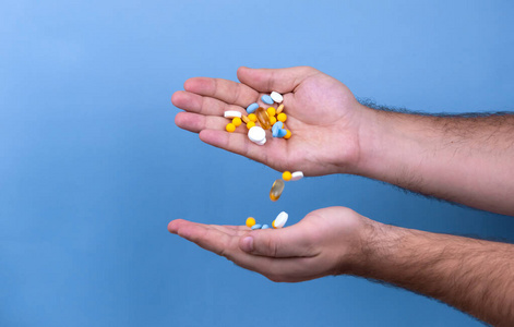 A pile of multicolored pills in a male hand. A man holds pills 