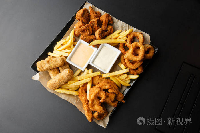 小吃拼盘奶酪条鸡块洋葱圈土豆块混合零食和酱汁啤酒板水平照片酒吧