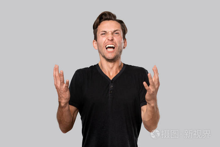 一个穿着黑色t恤的愤怒的男人在灰色背景下大声喊叫着孤立