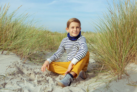 一个英俊的少年男孩坐在沙滩上的白色沙滩上
