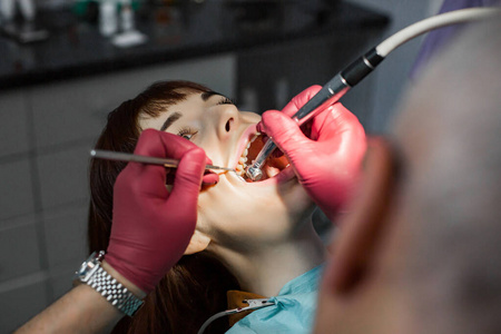 高级男牙医在牙科椅上为年轻女性患者钻孔