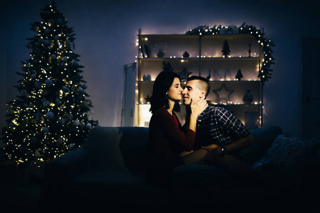 圣诞约会幸福,在黑暗中相爱的情侣,在沙发上的夜晚,黑暗的背景,圣诞树