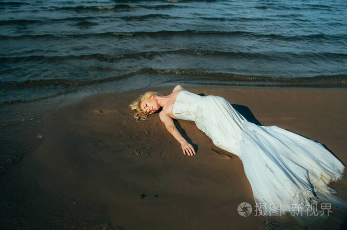 年轻金发新娘的画像躺在水里的沙滩上