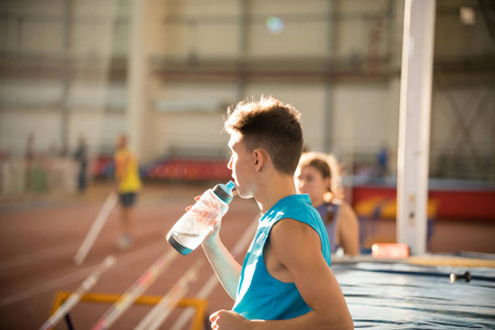 一个穿着蓝色衬衫的年轻人站在体育馆里喝着瓶子里的水