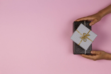 手拿着礼物纸包裹在浅粉色背景上的礼物。圣诞节新年假日概念
