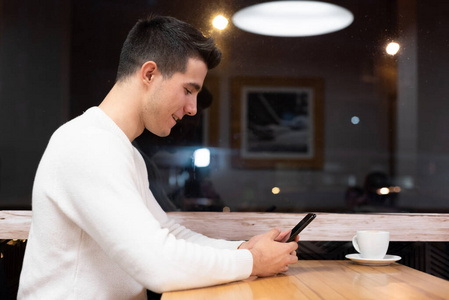 年轻英俊的白人男子坐在咖啡厅用手机喝咖啡。白人男性，喝着咖啡，在智能手机上读短信。