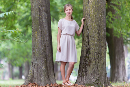 一位年轻女子在夏天站在树干旁的画像