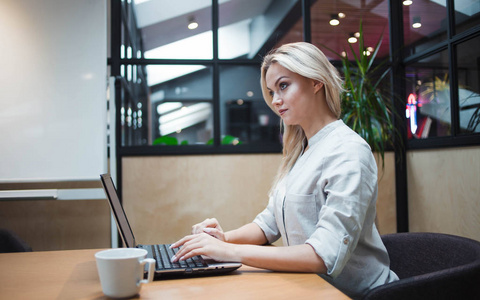 年轻自信的女人在办公室里用笔记本电脑工作。