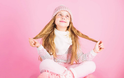 冬季时尚概念。女孩长发放松粉红色背景。孩子微笑时尚模特。小女孩戴着可爱的针织时尚帽子和舒适舒适的衣服。儿童冬季时装