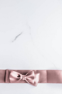 Beige silk ribbon and bow on marble background, glamour present 